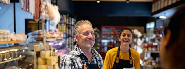 Two sales associates smiling at a customer in a cheese shop