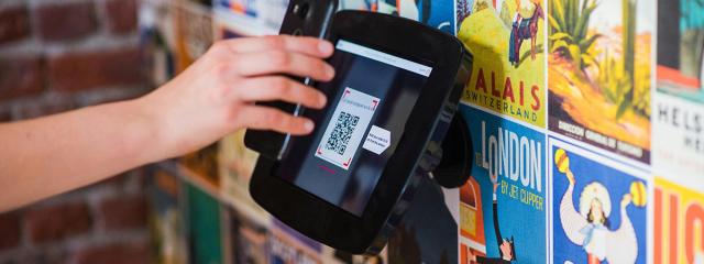 Phone held over payment terminal displaying QR code