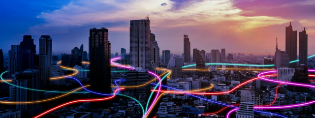 Twilight city skyline with glowing, multicolored light trails weaving through skyscrapers and streets.